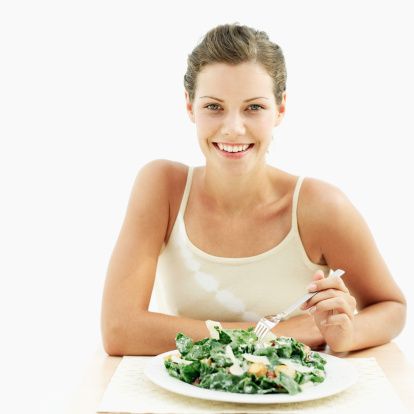 portrait of a young woman sitting with a plate of spinach